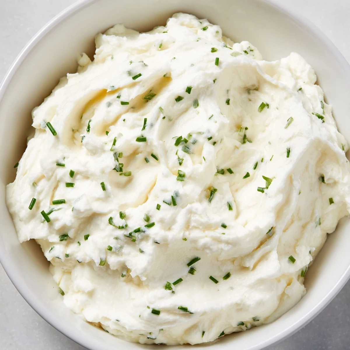 A close-up of the Creamy Appetizer Spread Dip topped with fresh chives, alongside gluten-free crackers and colorful vegetable sticks for dipping.
