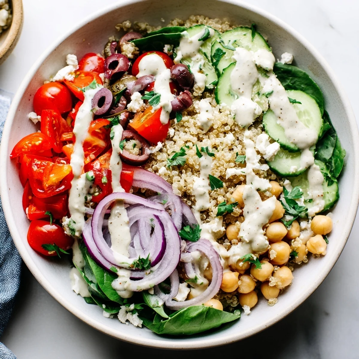 A vibrant Mediterranean Dinner Grain Bowl with quinoa, cherry tomatoes, cucumber, and feta, drizzled with creamy lemon-tahini dressing.  