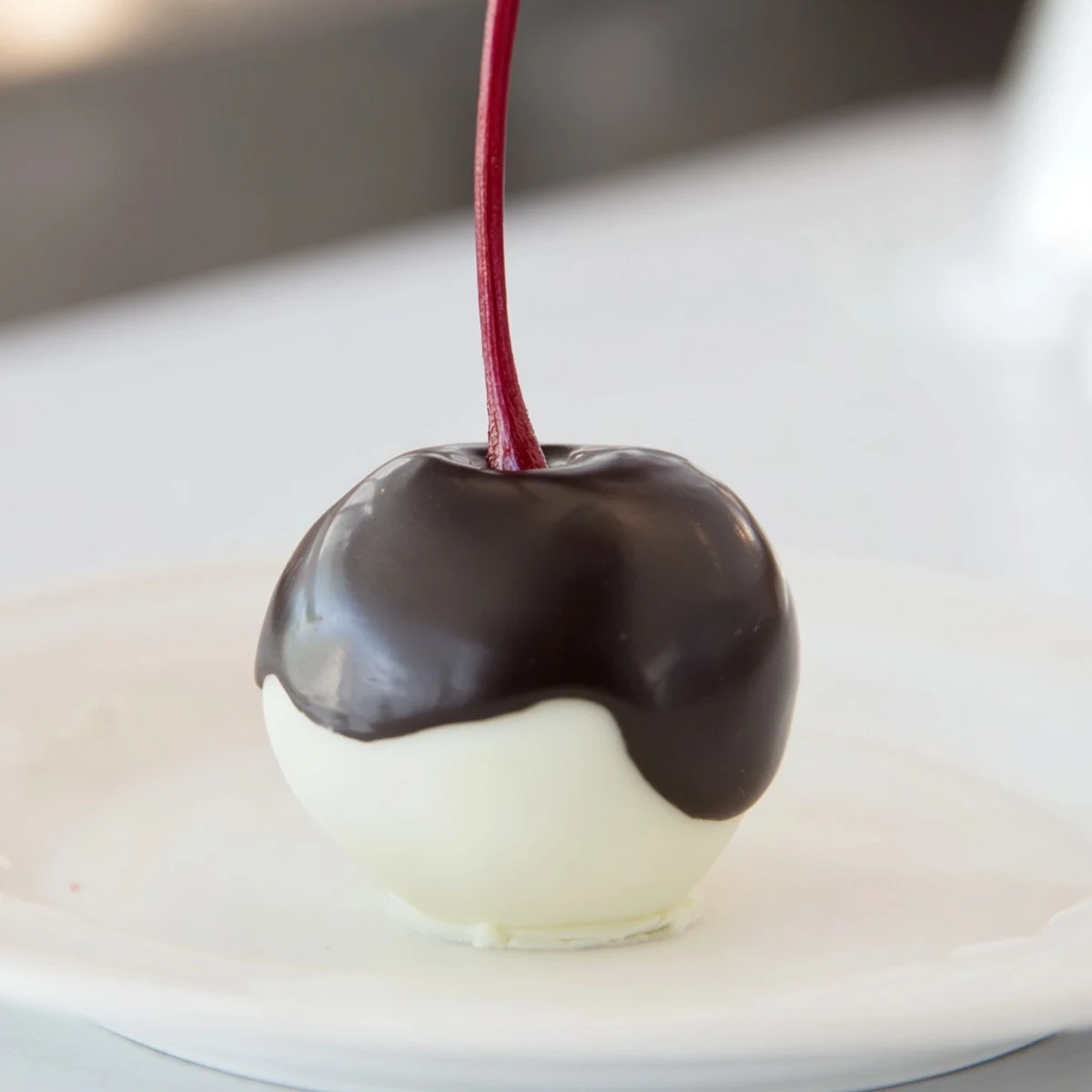 Glossy chocolate-covered cherries with a creamy fondant center, displayed on a marble surface for a festive American treat.
