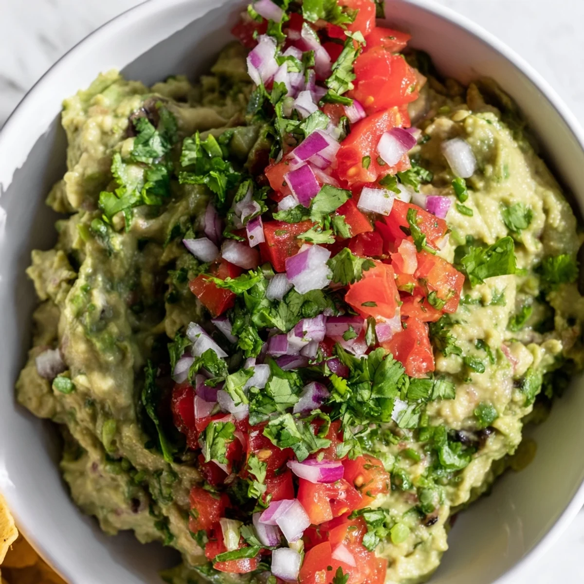 A vibrant bowl of creamy guacamole topped with fresh pico de gallo, served with crunchy tortilla chips for dipping.  
