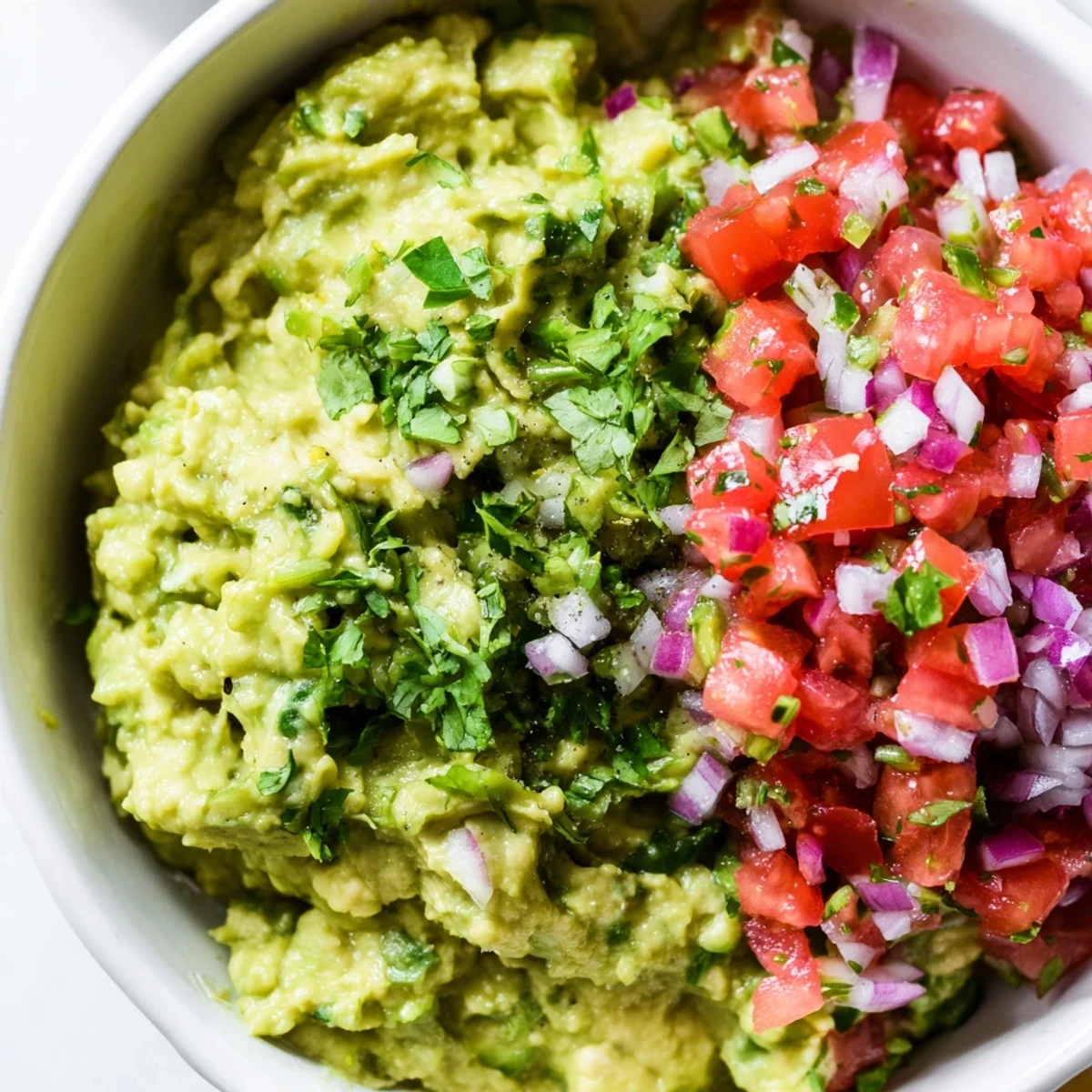 Freshly mashed guacamole with a zesty pico de gallo garnish, perfect for snacking or as a party appetizer dip.  