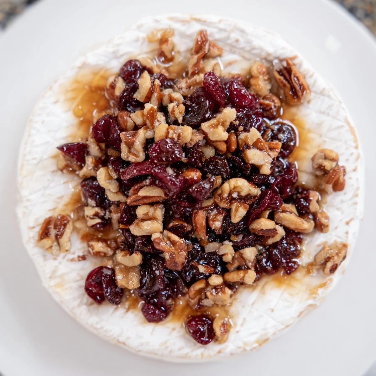 A baked wheel of Baked Brie with Cranberry and Pecan Topping bubbling on a rustic board, surrounded by crackers.