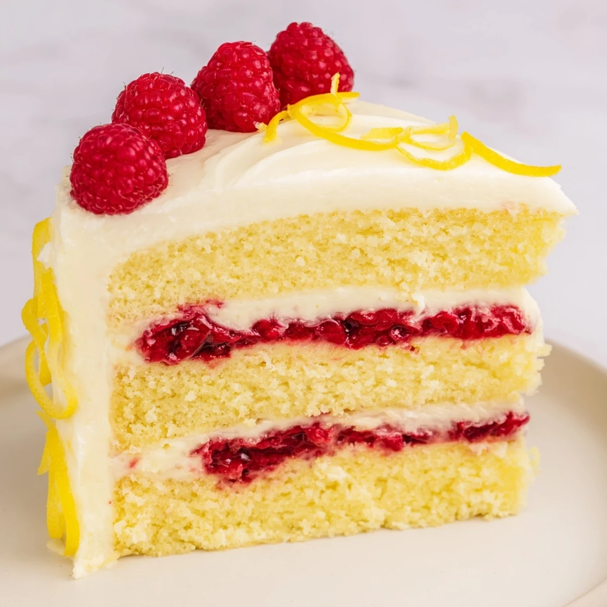 Moist Lemon Raspberry Layer Cake with Frosting displayed on a white cake stand, ideal for spring gatherings or birthdays.