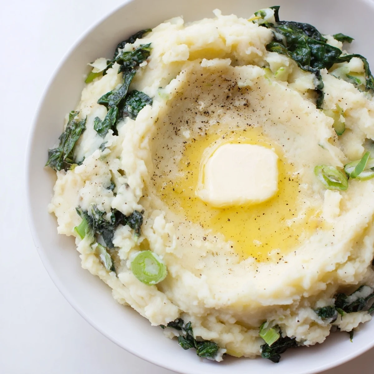 Golden mashed potatoes blended with sautéed kale and melting butter in a rustic bowl.