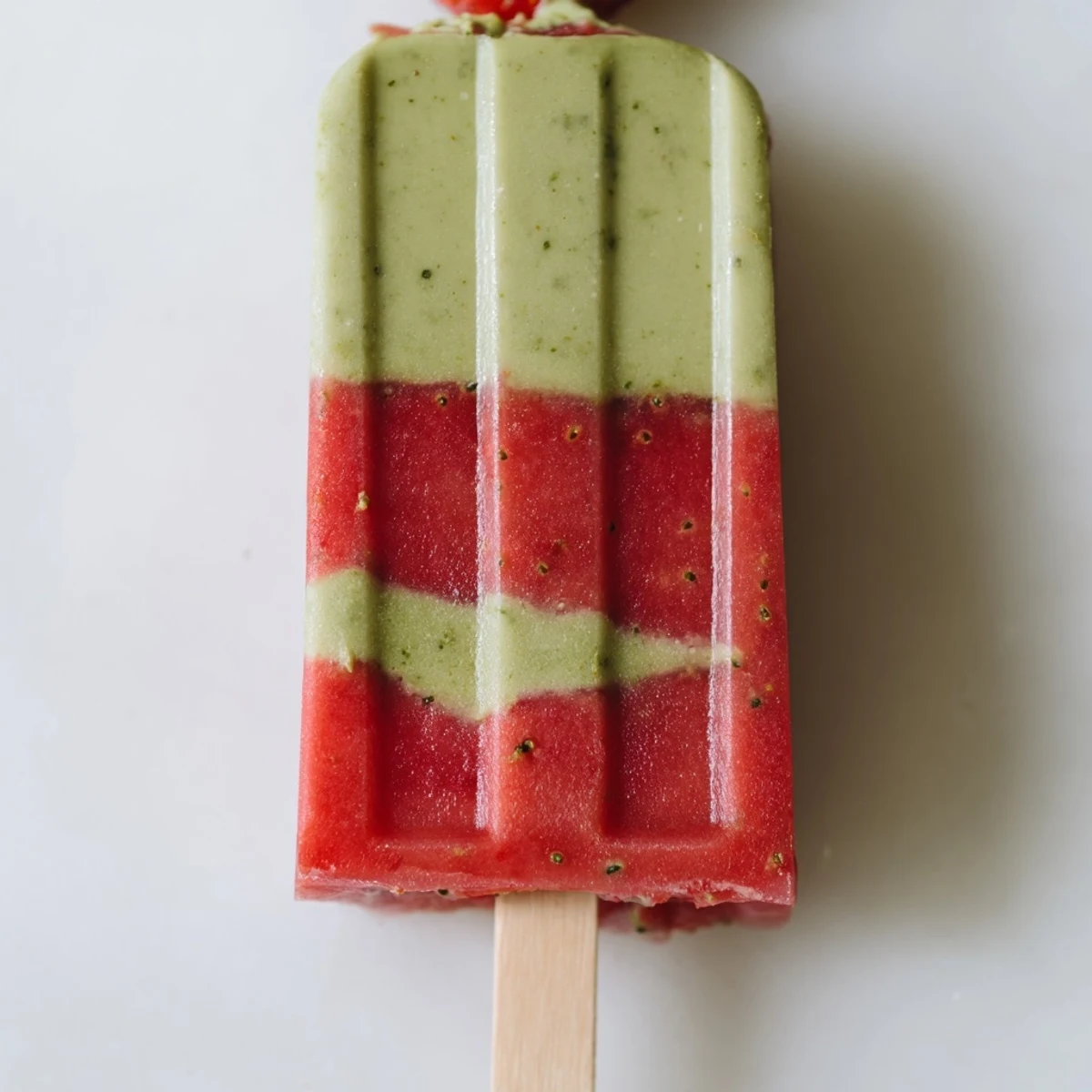 Homemade Strawberry Matcha Latte Popsicles on a wooden tray with fresh berries and mint for a summer treat.