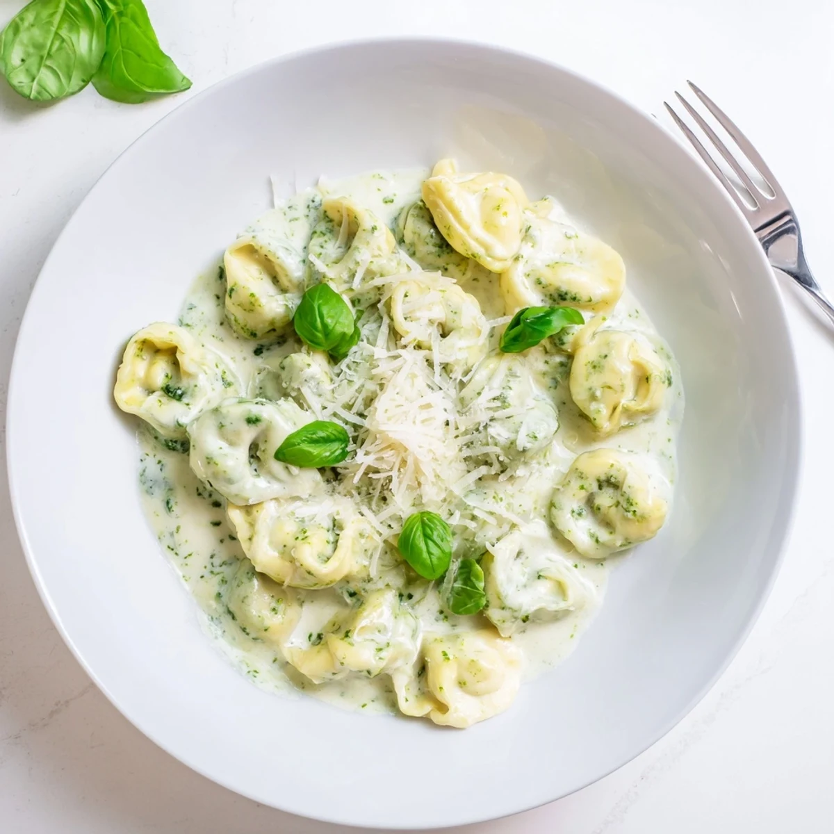 A skillet of Pesto Alfredo Tortellini topped with basil leaves and grated Parmesan, paired with garlic bread.