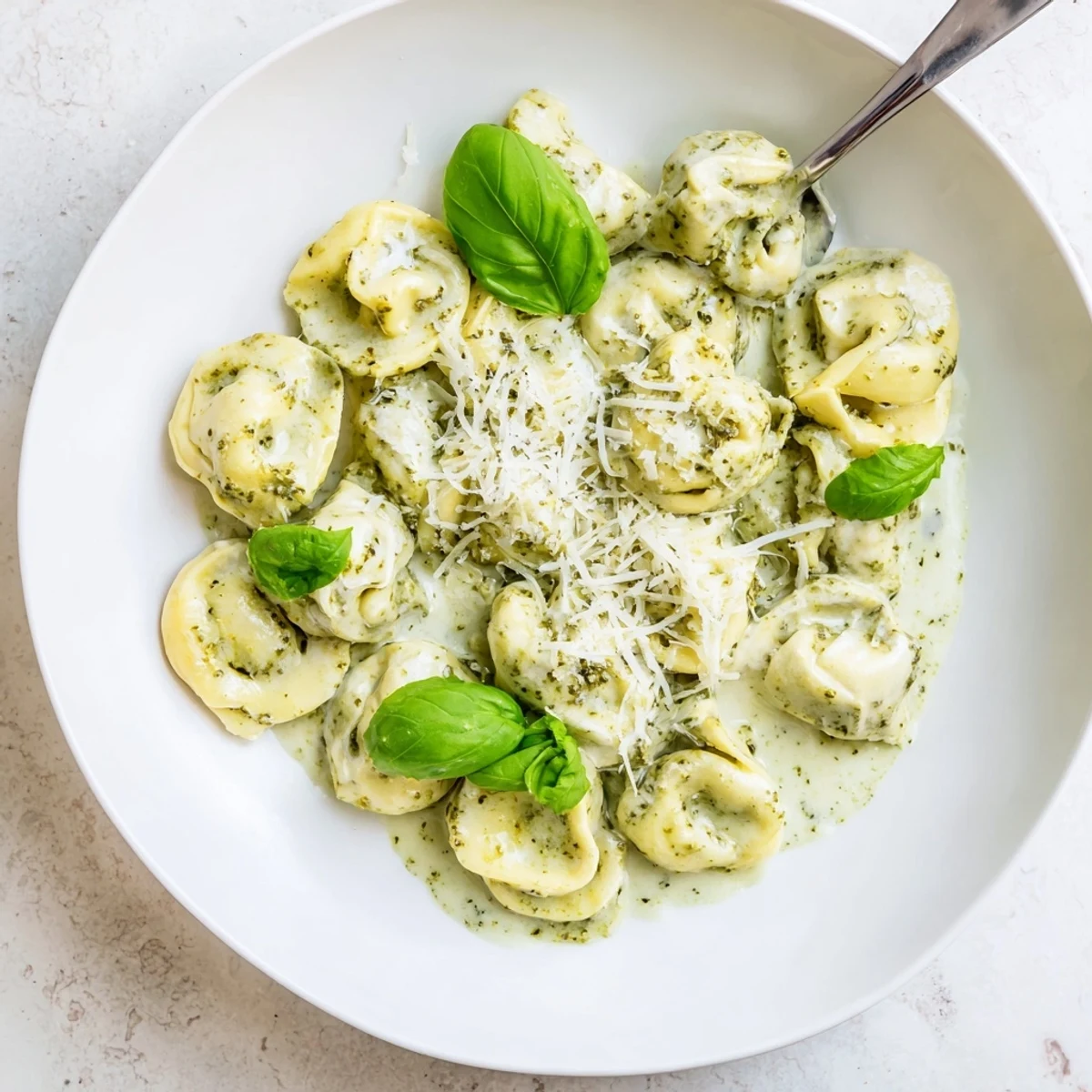 Steaming cheese tortellini glistens in creamy Pesto Alfredo Tortellini, garnished with fresh basil and pine nuts.