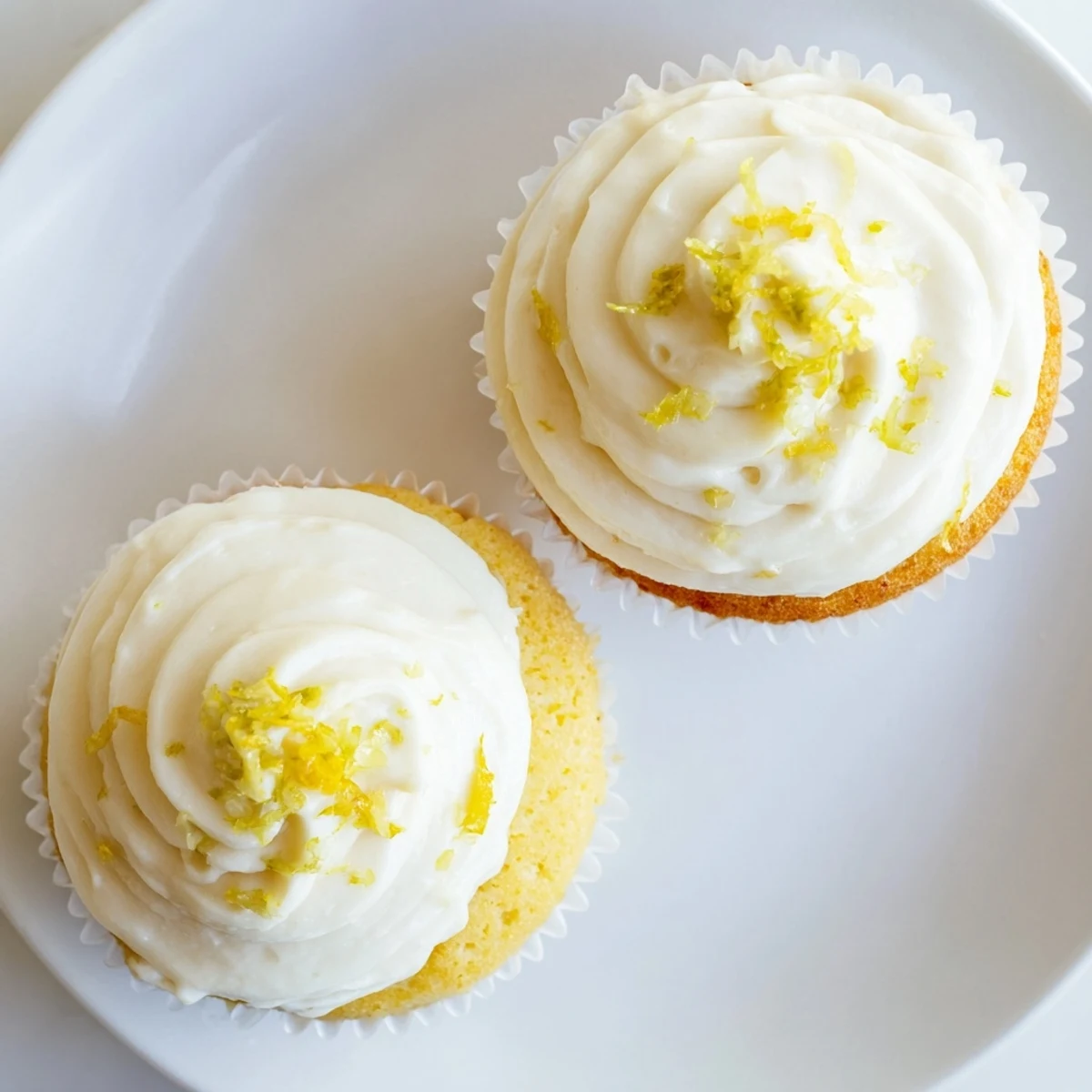 Freshly baked Limoncello cupcakes with creamy frosting on a pastel plate, surrounded by lemon slices and zest for a bright, summery vibe.