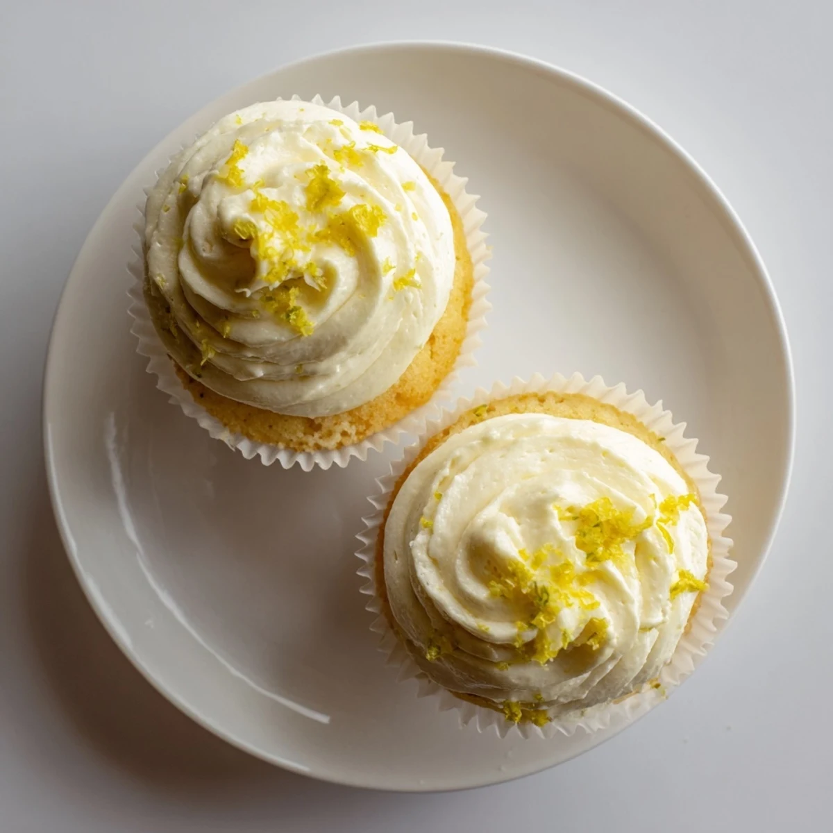 Delicious Italian-inspired Limoncello cupcakes garnished with lemon zest, displayed on a marble countertop for an elegant dessert presentation.