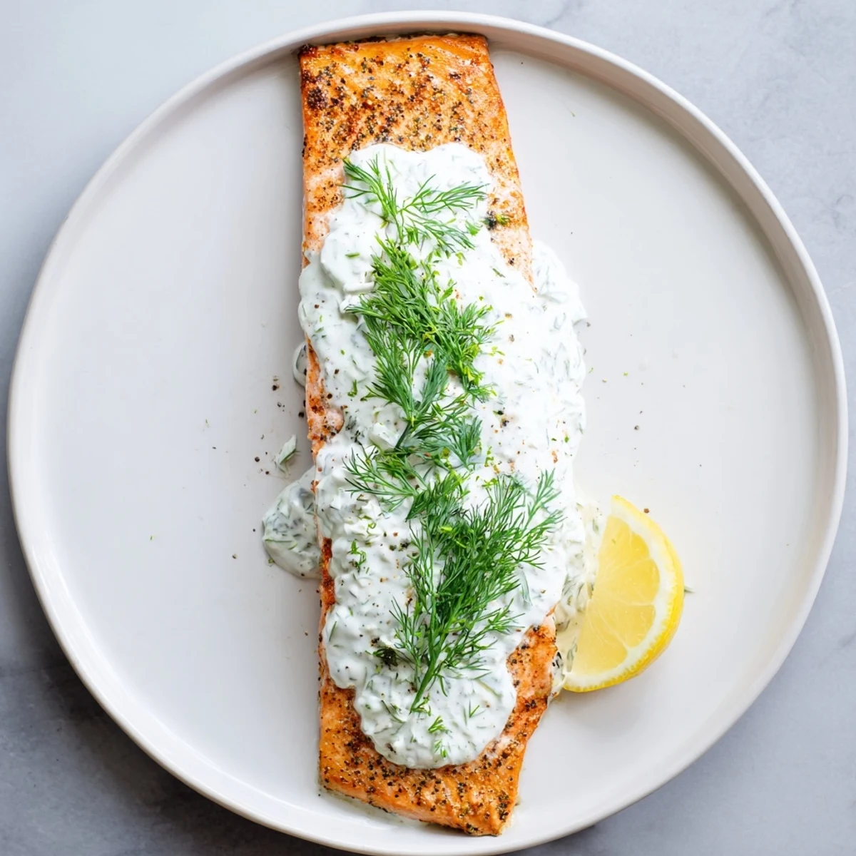 Perfectly baked Mediterranean salmon drizzled with herbaceous lemon dill yogurt on a white plate