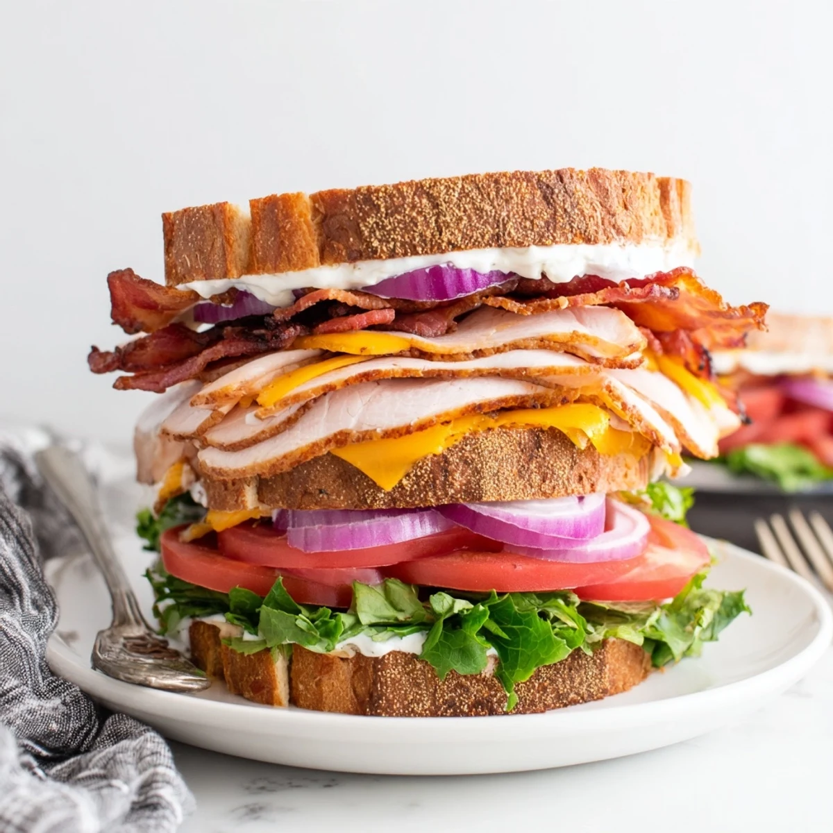 Stacked turkey beef bacon ranch sandwich featuring layers of meat, cheese, and crisp vegetables on toasted golden brown bread