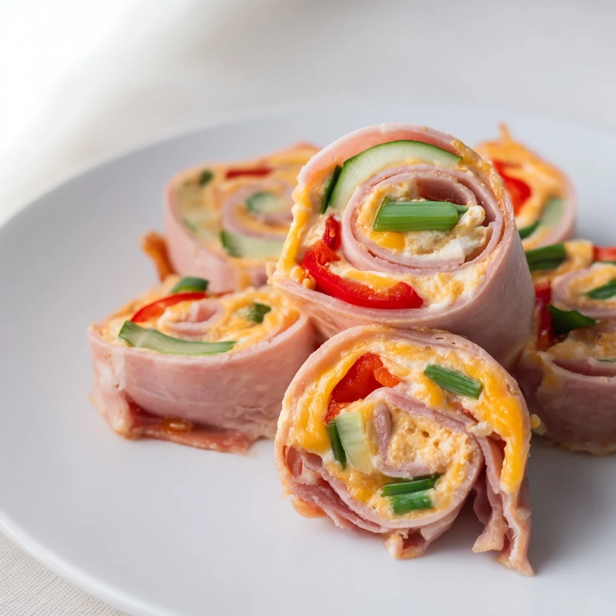 Low-carb keto ham roll ups arranged neatly with fresh cucumber and red bell pepper peeking through
