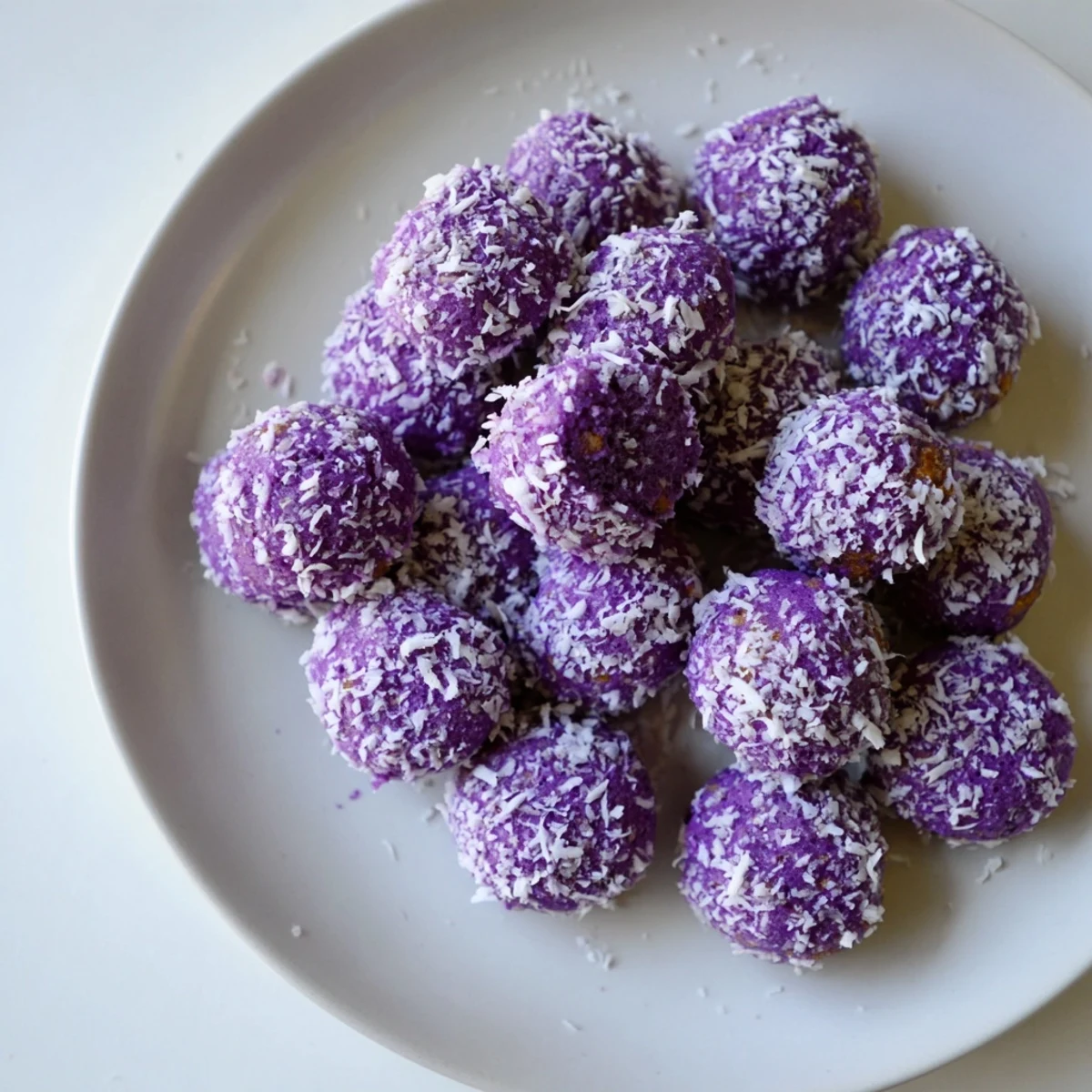 Golden coconut ube besito cookies arranged on a white serving plate, showing their vibrant purple center and snowy outer coating