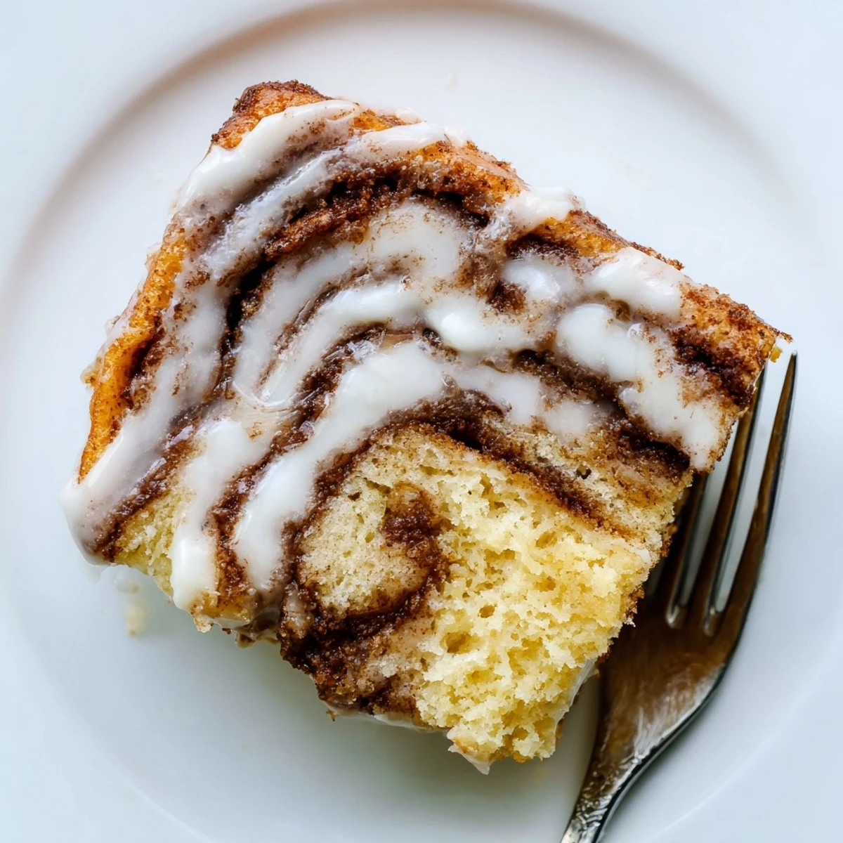 Golden swirled cinnamon roll cake with ribbons of spiced sugar beneath a silky white glaze