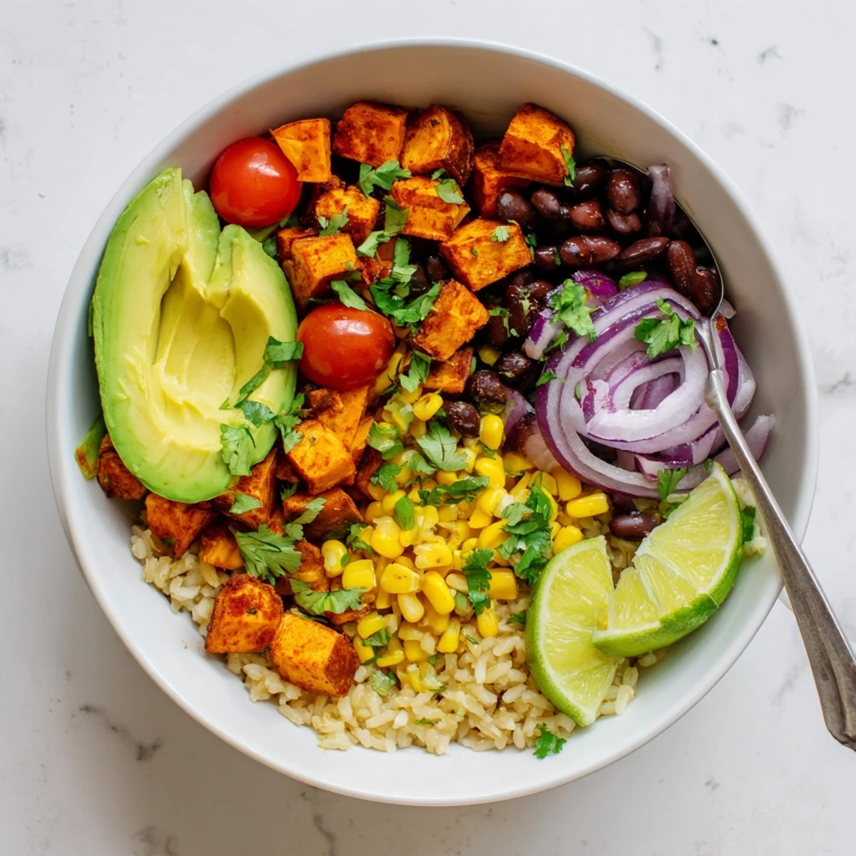Colorful vegan sweet potato burrito bowl topped with fresh avocado and zesty lime