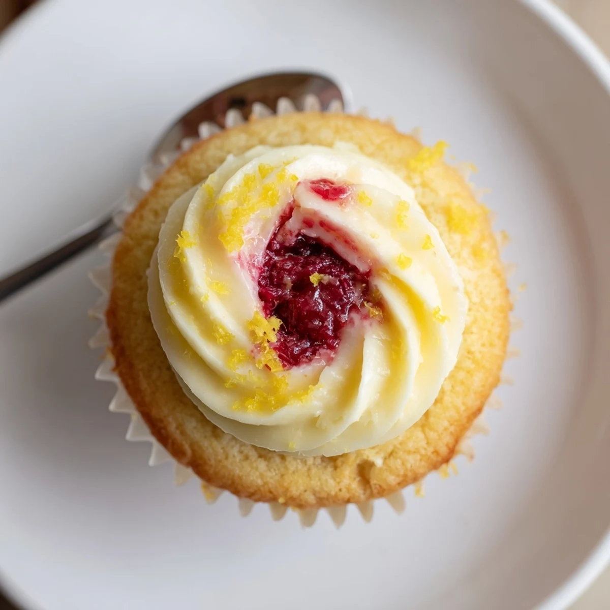 Golden lemon cupcakes topped with fluffy buttercream and filled with sweet raspberry preserves