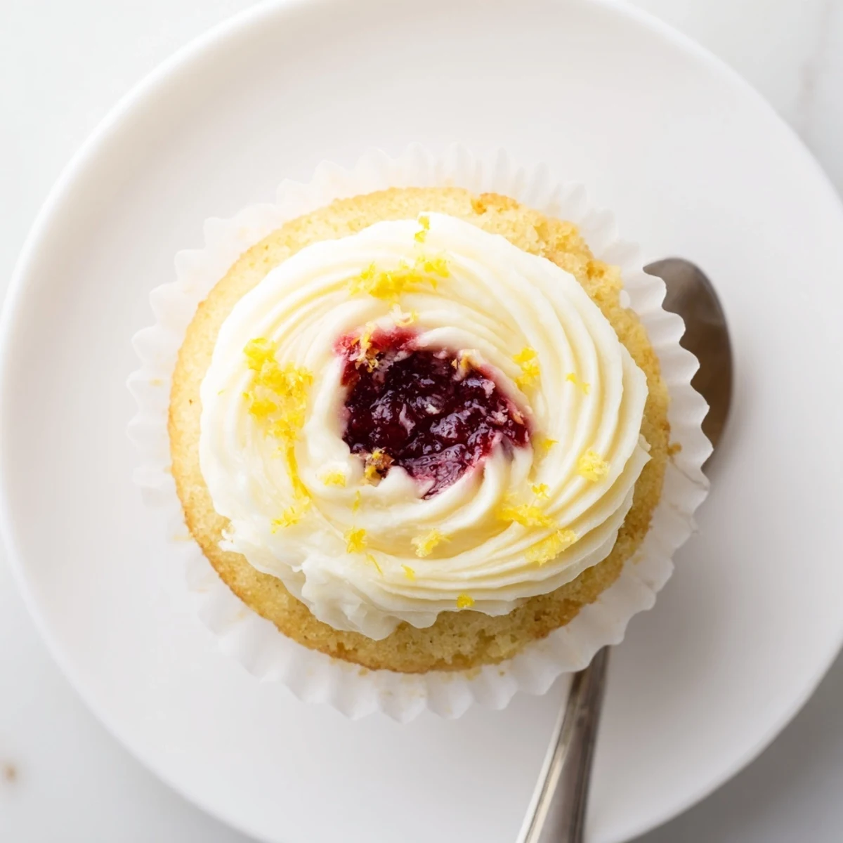 Fresh lemon cupcakes piped with buttercream frosting featuring a hidden raspberry jam filling inside