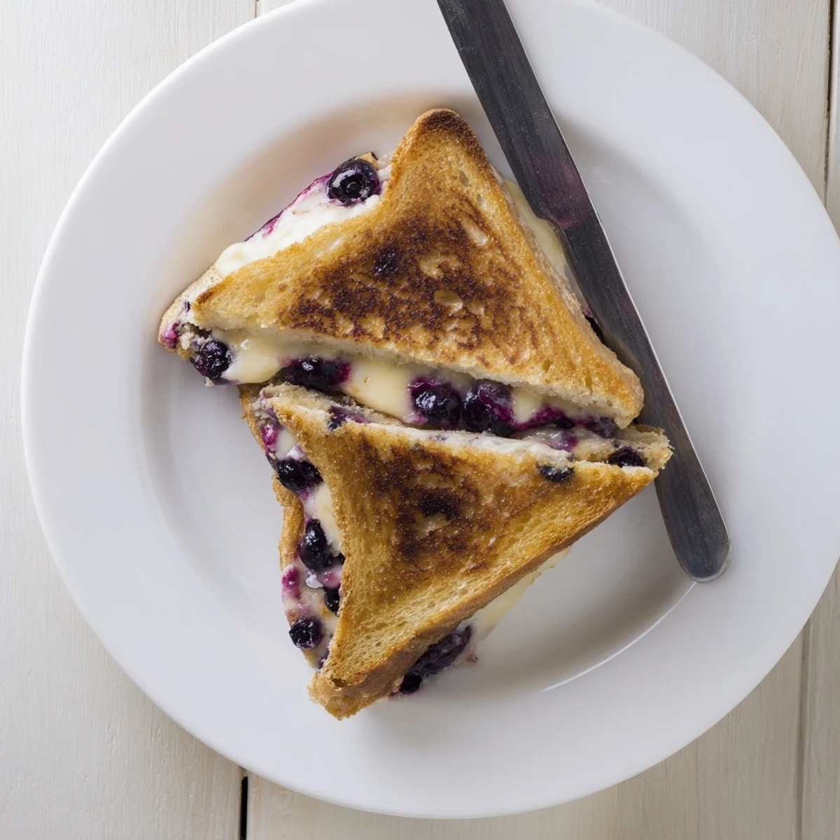 Golden blueberry grilled cheese sandwich with melted cheddar and burst blueberries on a plate