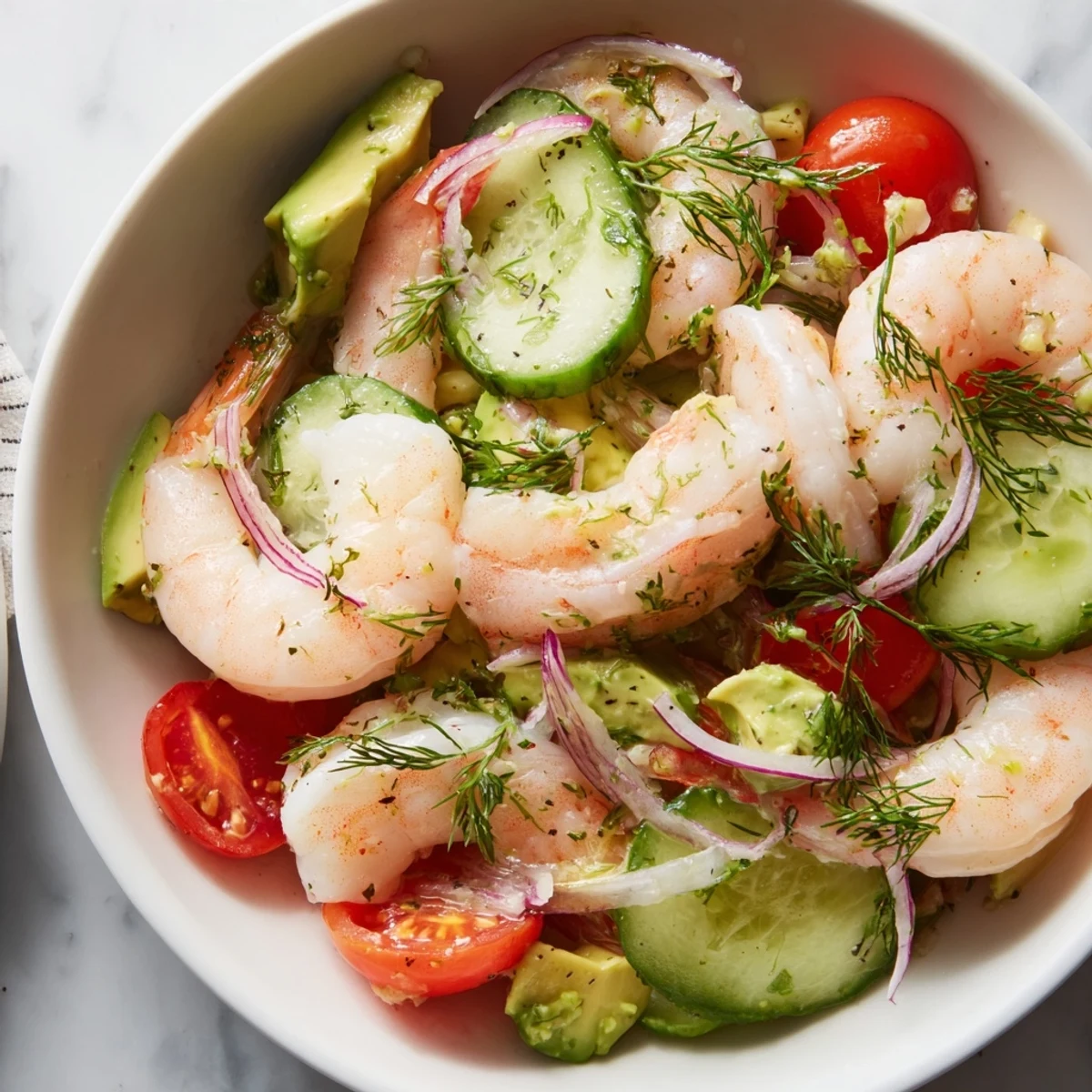 Vibrant cucumber shrimp salad bowl with juicy cherry tomatoes, red onion, and dill-topped seafood in a light olive oil dressing