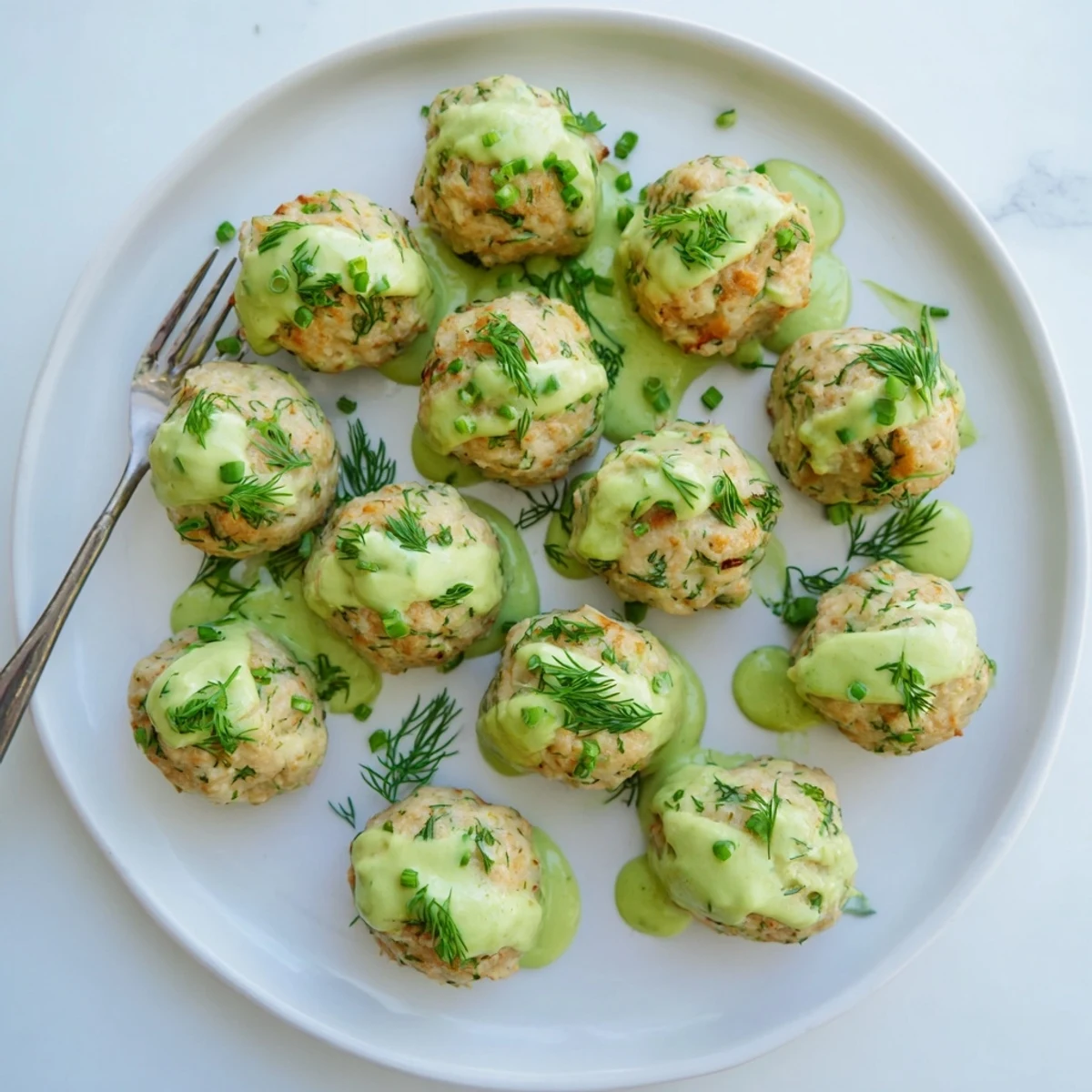 Plump salmon meatballs fresh from the oven served alongside a bowl of creamy zesty avocado dipping sauce