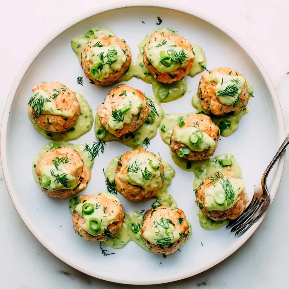 Close up of tender baked salmon meatballs garnished with fresh herbs and paired with smooth avocado sauce