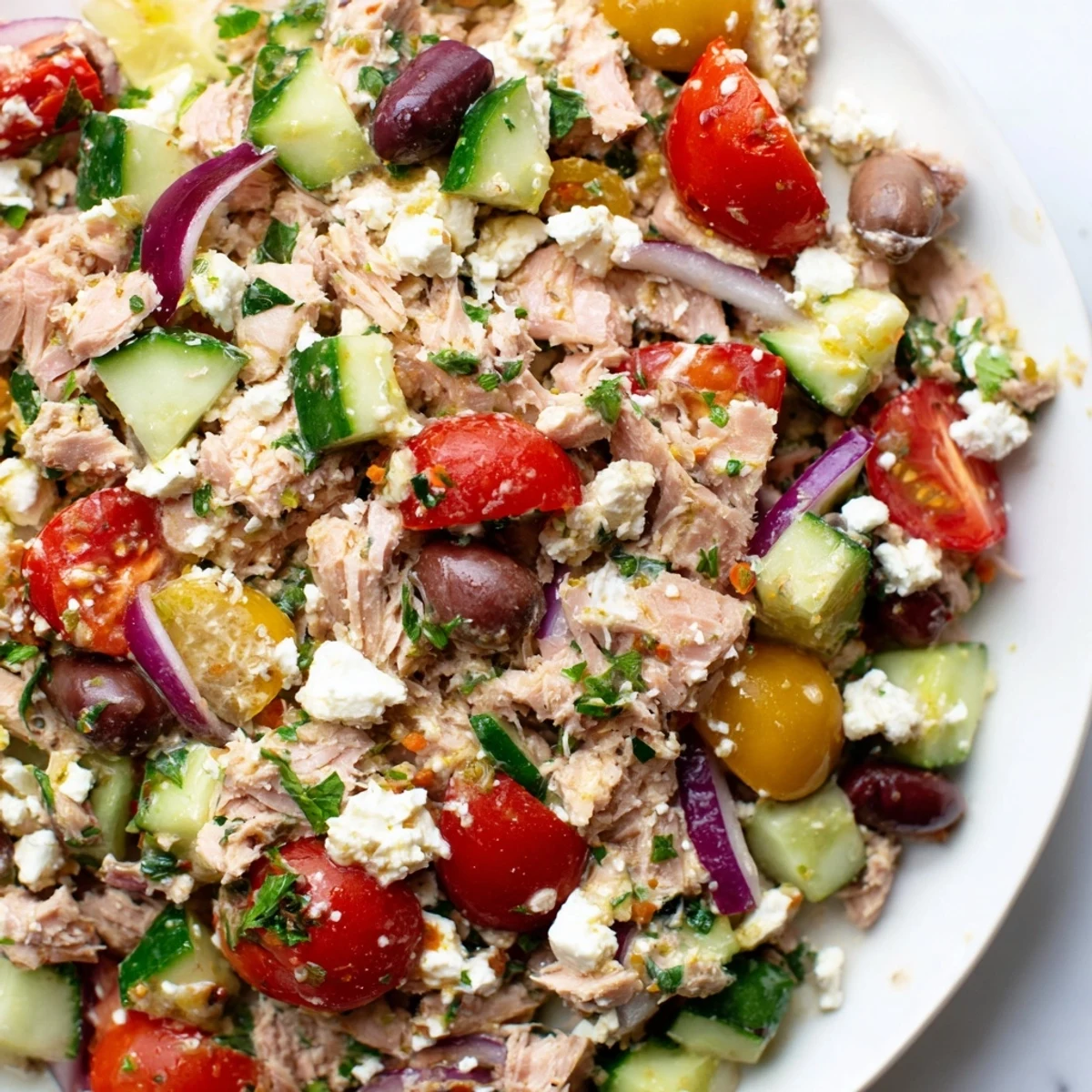 Colorful Mediterranean tuna salad bowl with fresh vegetables, olives, and lemon dressing served on white plate