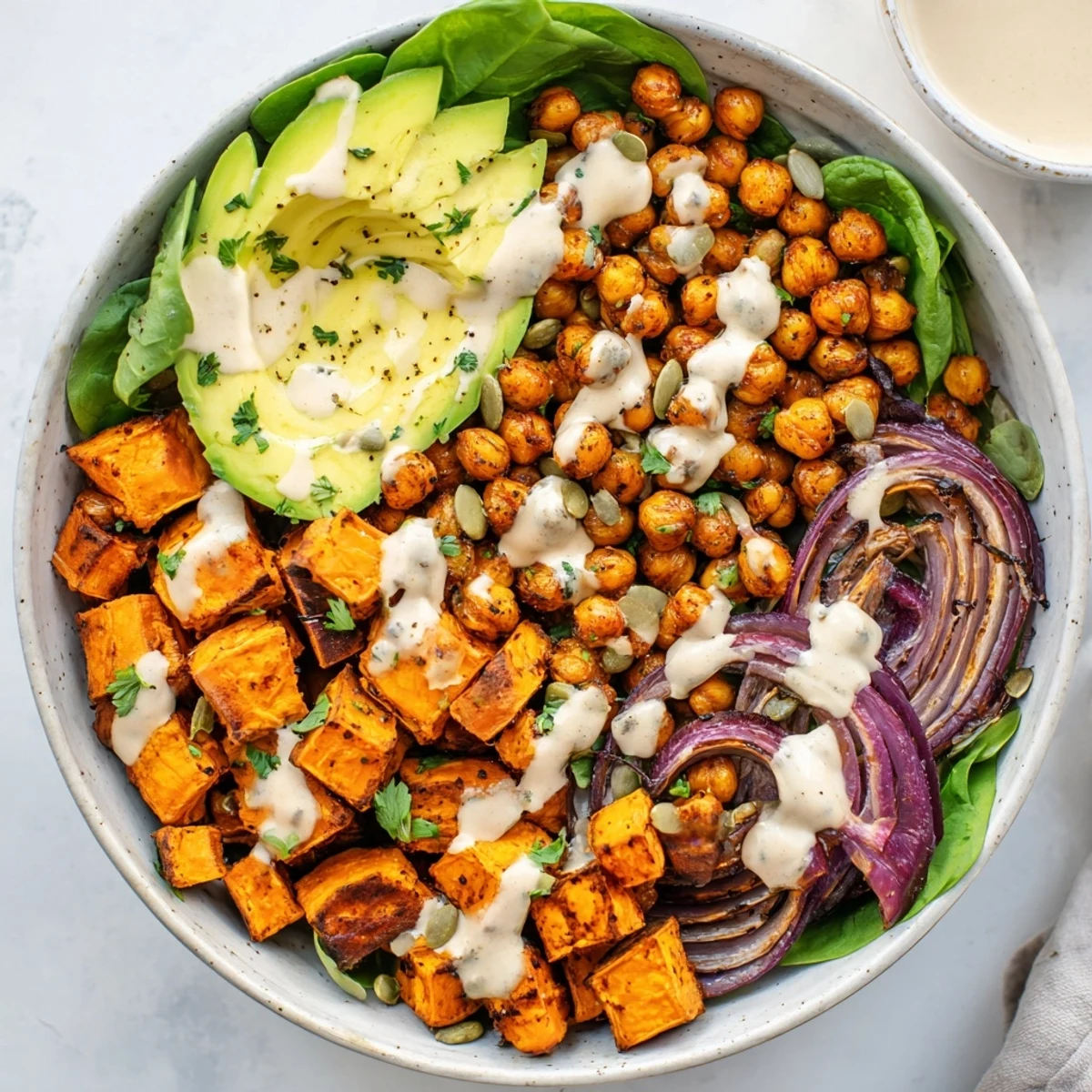 Colorful roasted sweet potato and chickpea bowls topped with creamy avocado and zesty tahini dressing over fresh greens