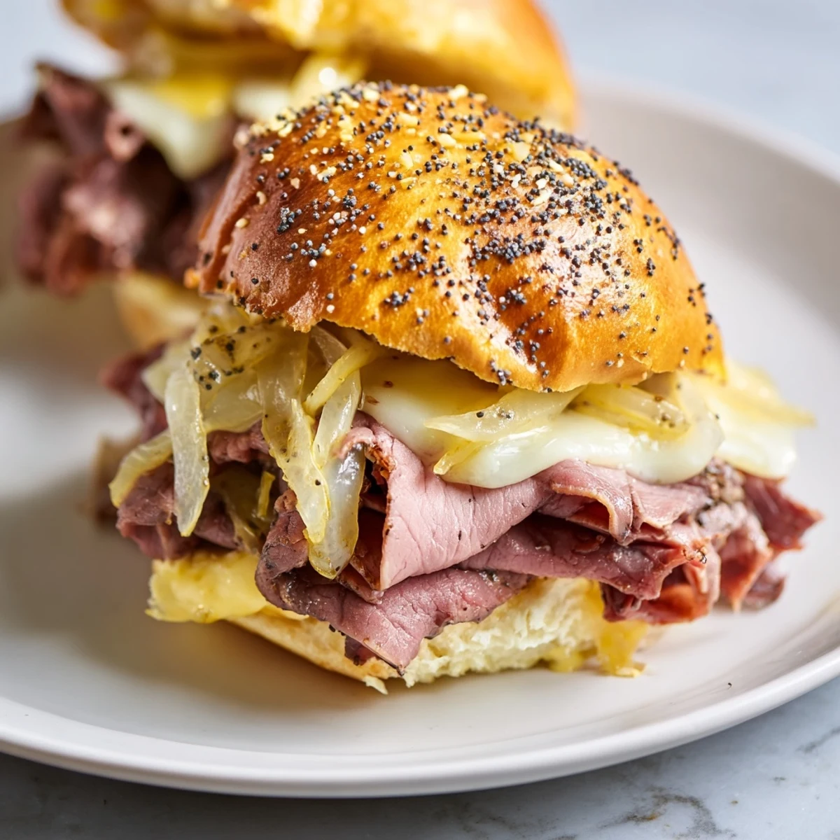Baked French dip sliders topped with poppy seeds alongside small bowls of savory dipping sauce