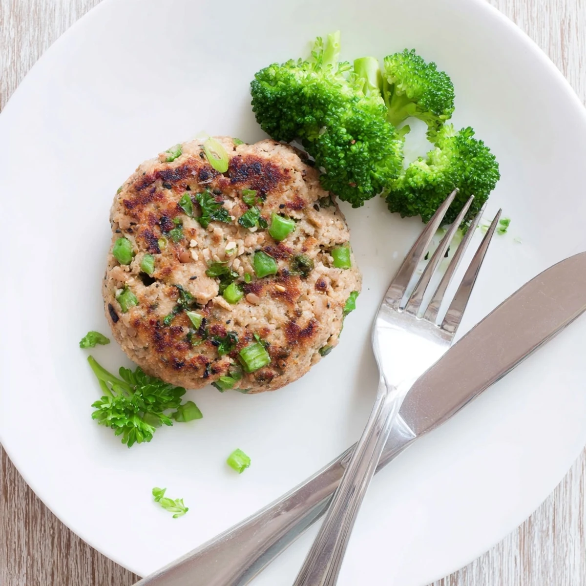 Golden brown turkey broccoli and quinoa burgers sizzling in a skillet with fresh green onion garnish