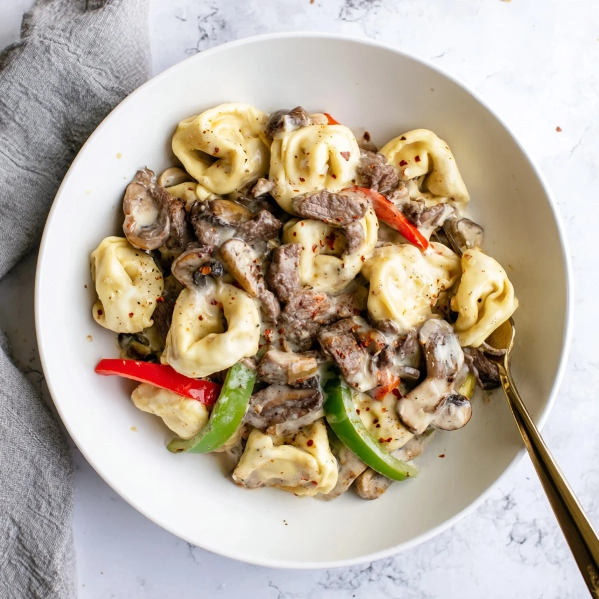 Slow cooker cheesesteak tortellini featuring sliced steak, cheese tortellini, and vegetables in a velvety cream cheese sauce.