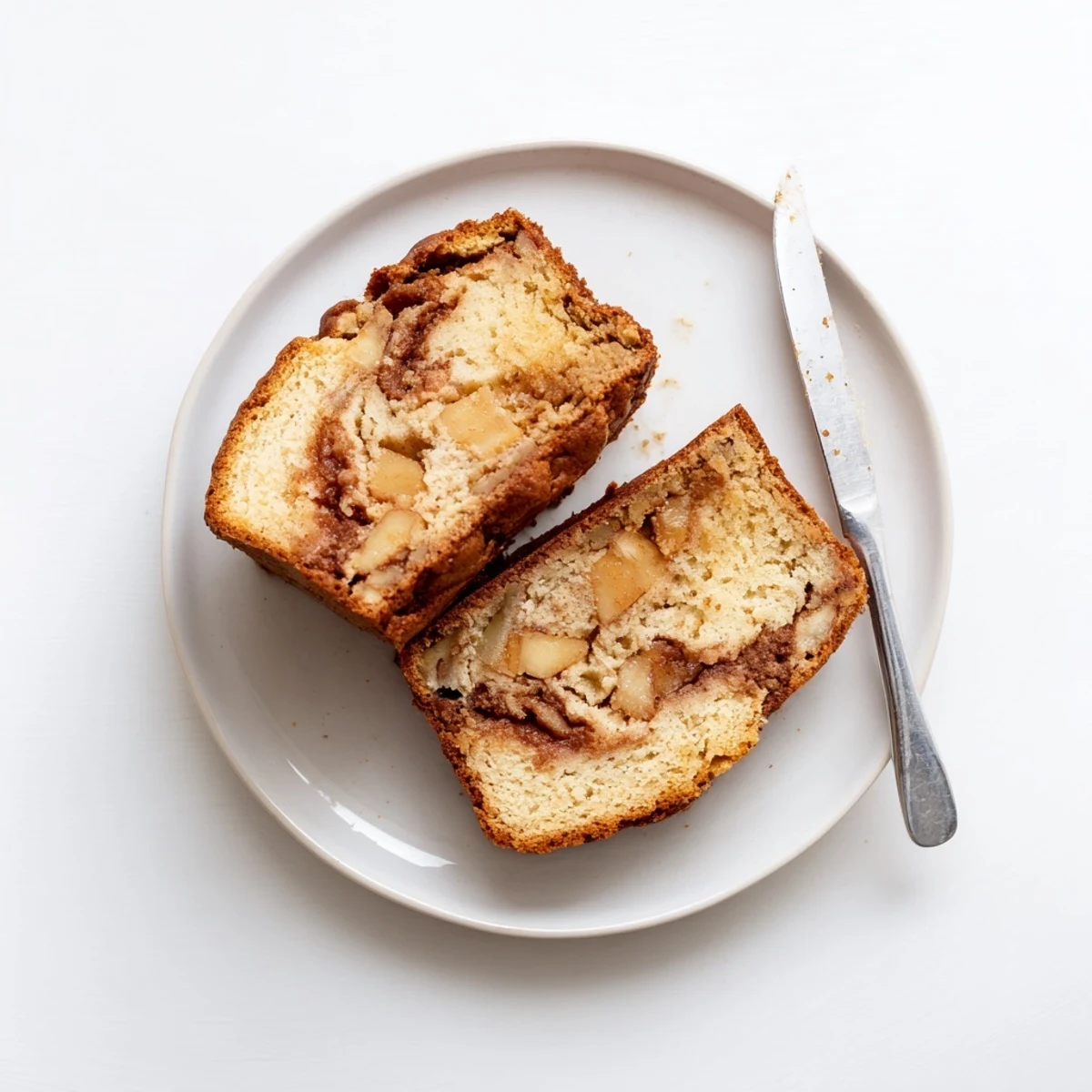Moist homemade cinnamon apple bread slice on a white plate with scattered diced apples