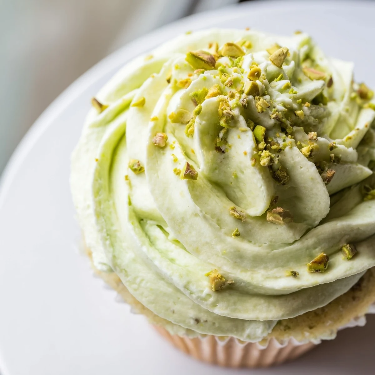 Moist pistachio cupcakes topped with swirled buttercream and sprinkled chopped nuts on striped napkin