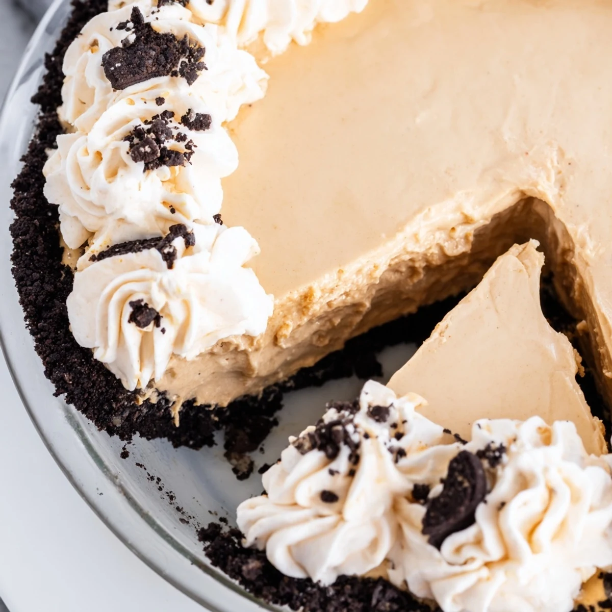 Creamy peanut butter Oreo pie sliced and topped with whipped cream and cookie crumbles
