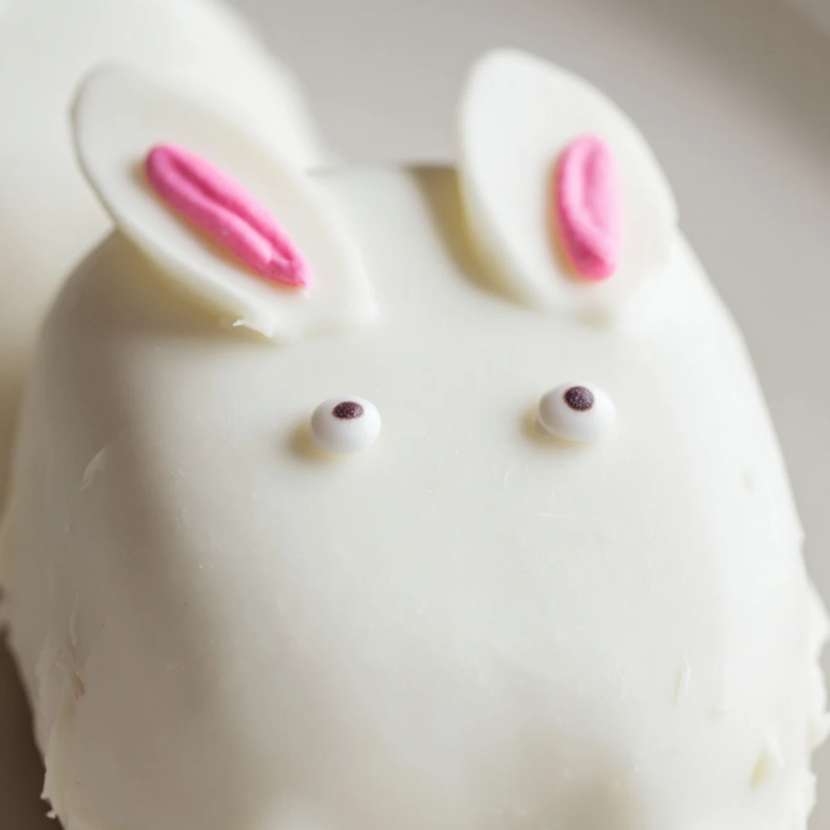 Adorable white chocolate bunny cakesicles with candy eyes and pink ears on a festive tray
