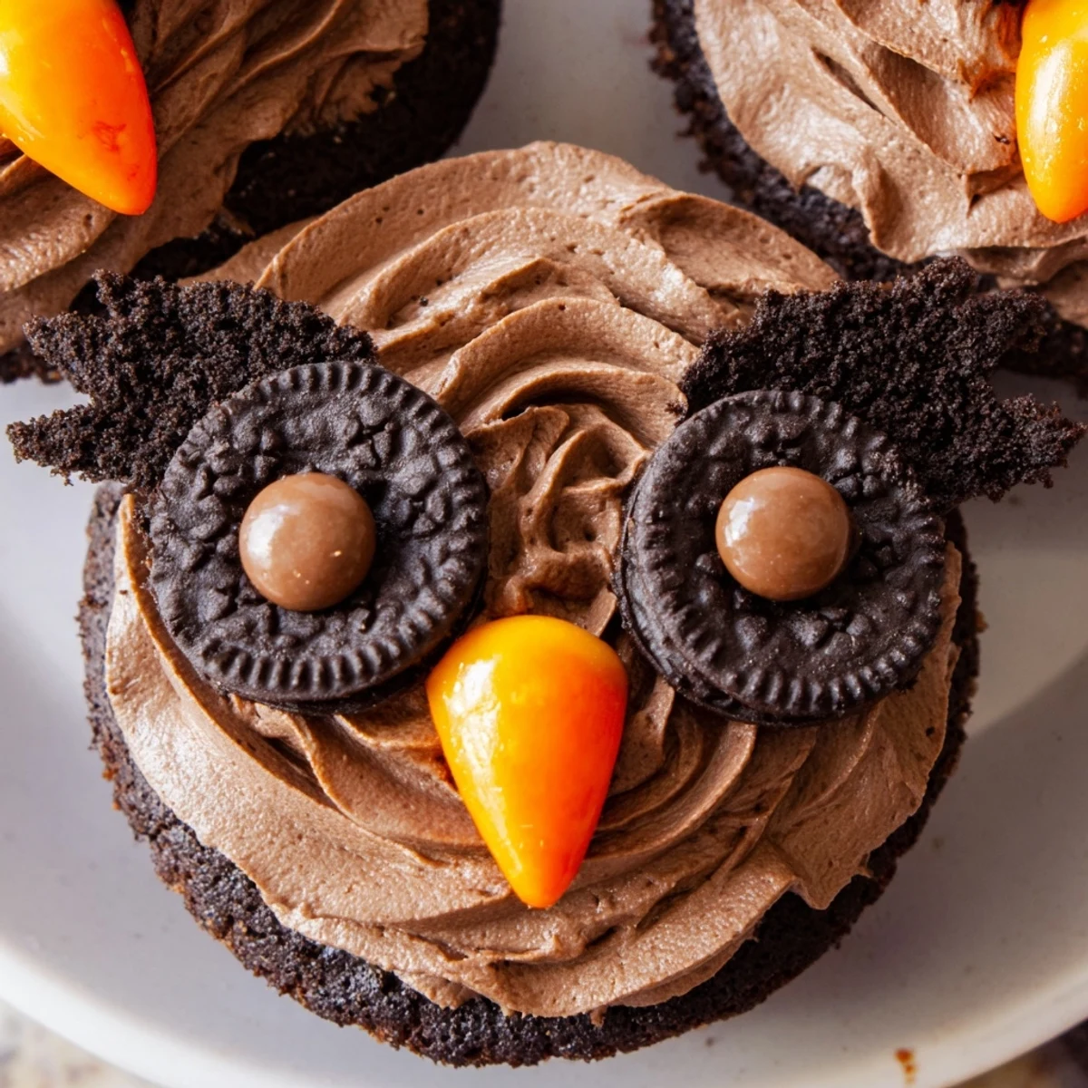 Close-up of Oreo Owl Cupcakes showing playful cookie eyes, orange candy beaks, and fluffy cocoa frosting piped high.