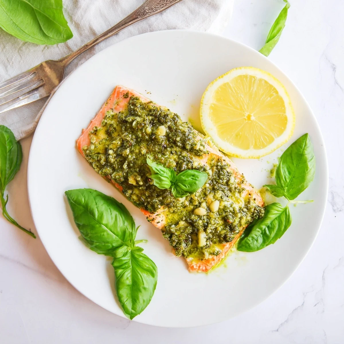 Golden baked pesto butter salmon fillet with herby green topping and fresh lemon garnish on white plate