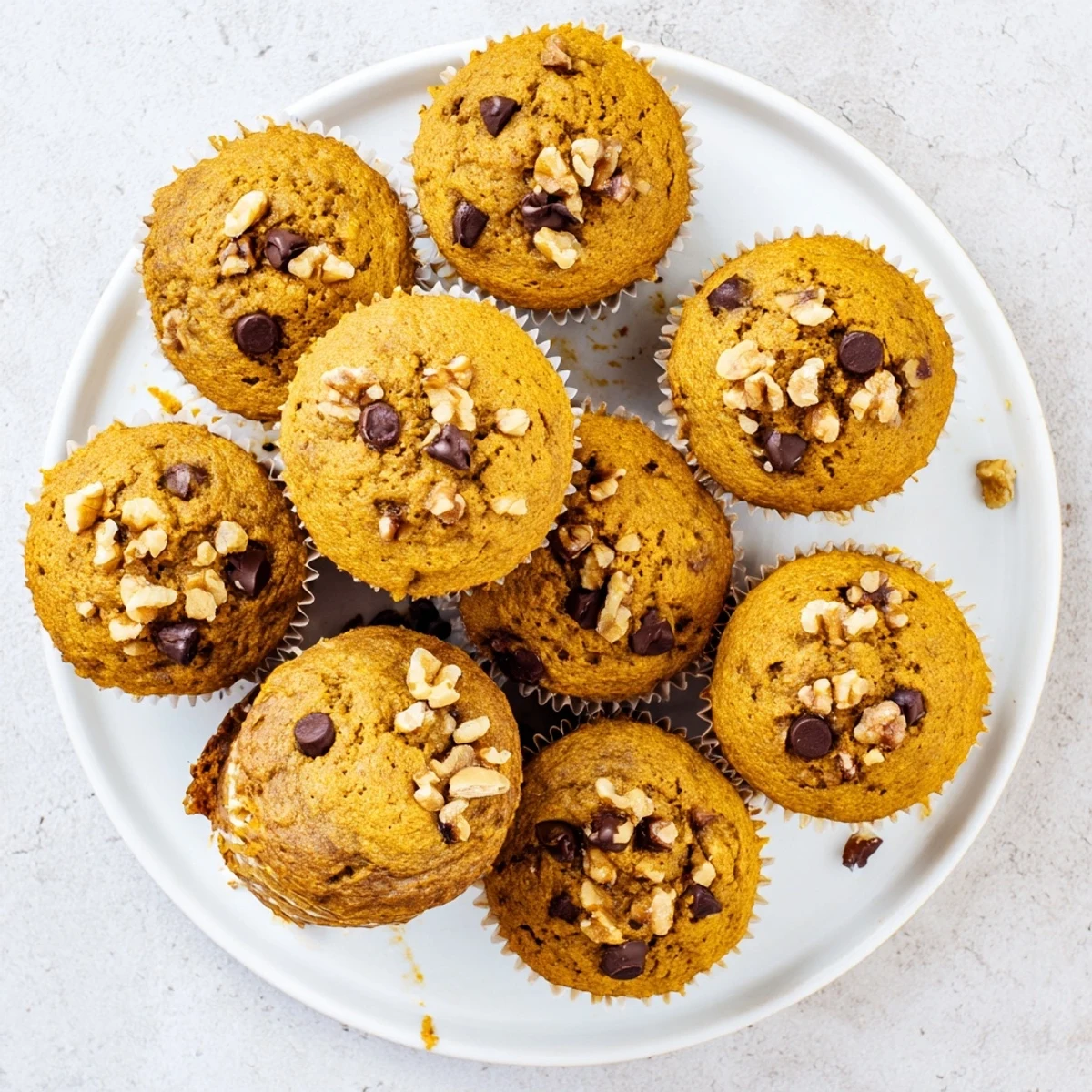 Golden butternut squash banana muffins topped with walnuts on a wooden board