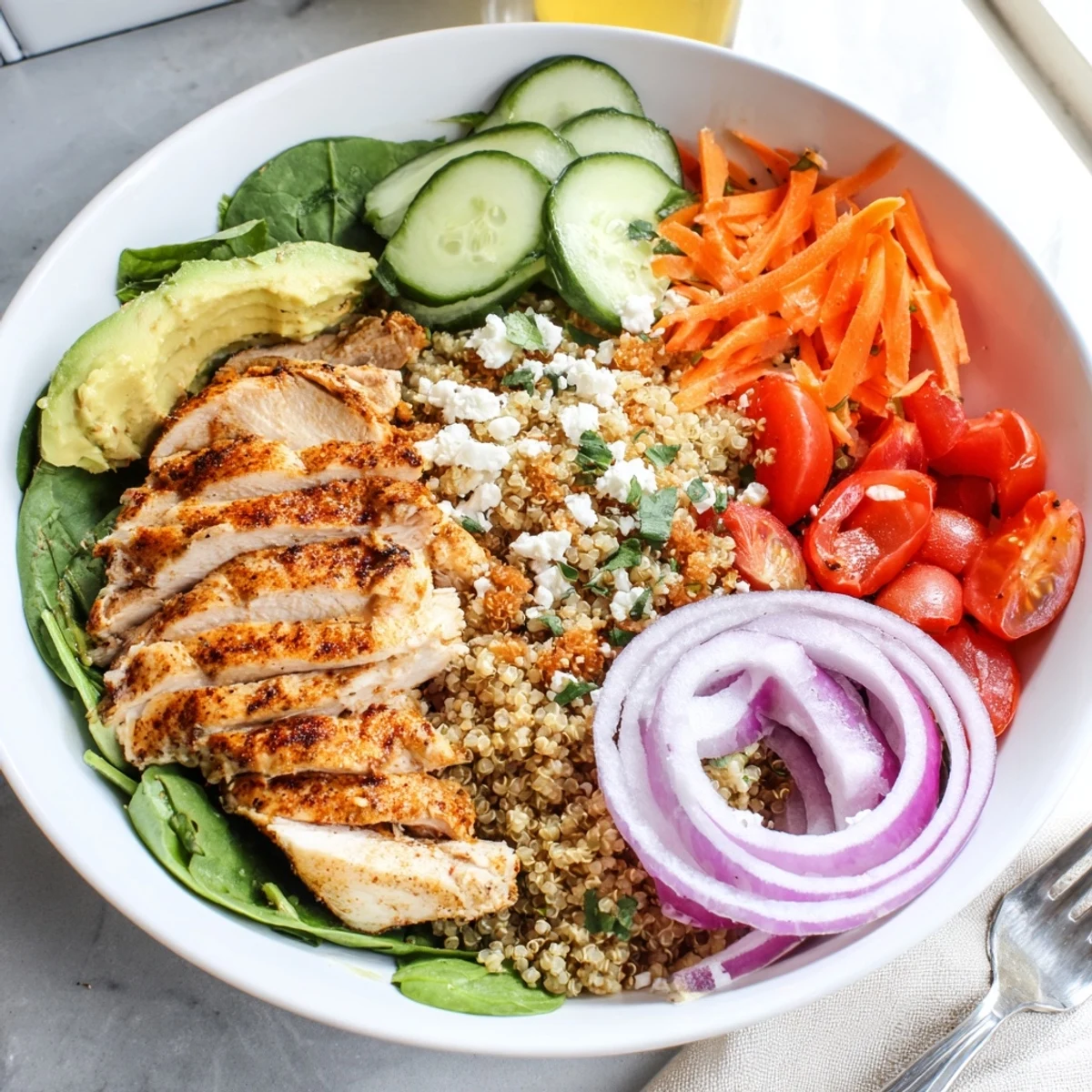 A colorful chicken grain bowl with sliced avocado, cherry tomatoes, and fluffy quinoa.