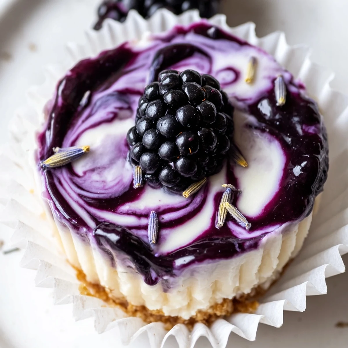 Creamy no bake mini blackberry lavender cheesecakes topped with glossy berry sauce in paper liners