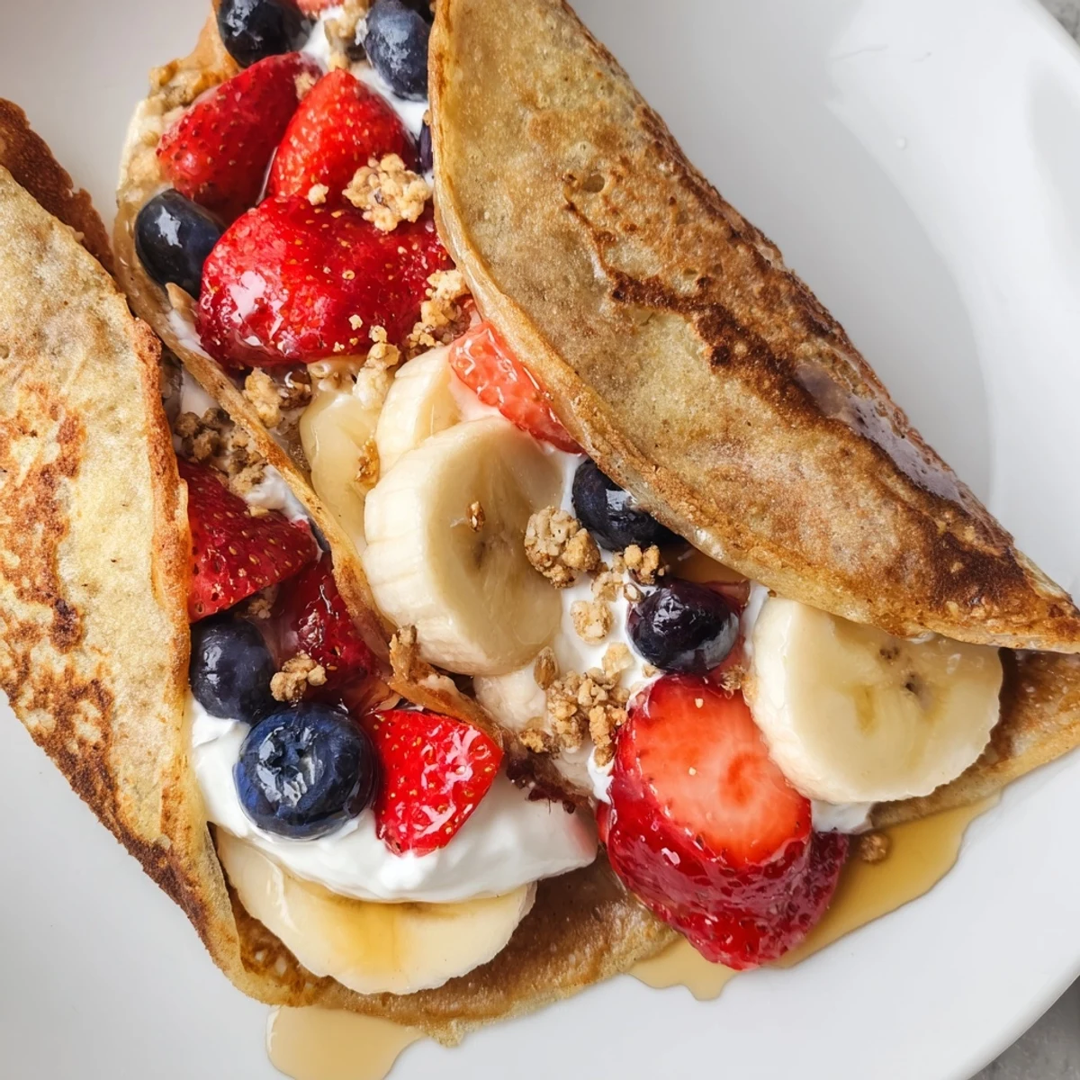 Golden pancake tacos stuffed with fresh strawberries and drizzled maple syrup on a plate