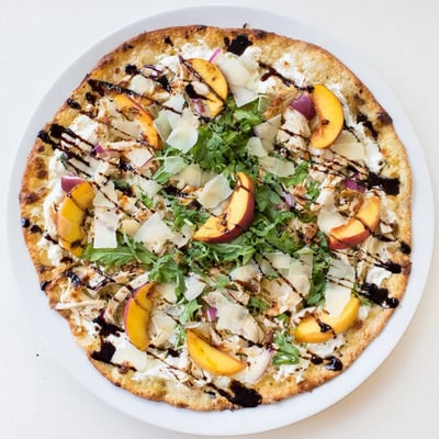 Summer-inspired chicken peach ricotta pizza featuring bubbling cheese and peppery greens on crisp crust