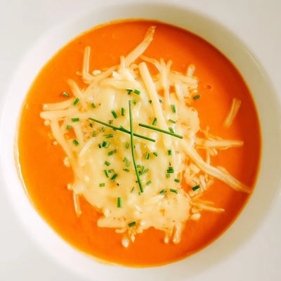 Velvety orange roasted red pepper and smoked Gouda soup sprinkled with shredded cheese