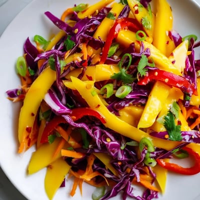 Fresh mango slaw served in white bowl featuring julienned vegetables, tangy lime dressing, and chopped peanut topping
