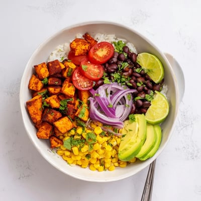 Roasted sweet potato burrito bowl piled high with black beans, corn, and creamy avocado