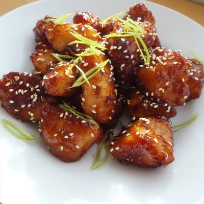 Juicy spicy honey sriracha chicken tossed in a glossy honey sriracha glaze with sesame seed garnish